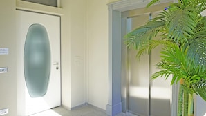 Un couloir avec une porte en verre dépoli, un interrupteur fixé au mur et un palmier en pot.
