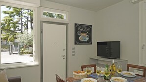 Un coin repas avec une table dressée pour deux personnes, un téléviseur placé au-dessus de la table et une fenêtre donnant sur des arbres et des bâtiments.