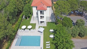 Vue aérienne d’une maison moderne à deux étages, dotée d’une piscine, entourée d’une végétation luxuriante et comprenant un espace de stationnement.