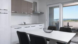 A modern kitchen with white cabinets, a stainless steel range hood, and a dining area with a white table and black chairs. - Apartment Franka by Interhome (Trogir)