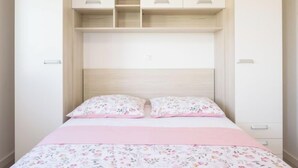 A bedroom with a bed, two pillows, a pink bedspread, and a white wardrobe with open shelves. - Apartment Franka by Interhome (Trogir)