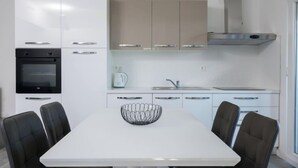A modern kitchen with white cabinets, a black oven, a stainless steel range hood, and a white dining table with four chairs. - Apartment Franka by Interhome (Trogir)