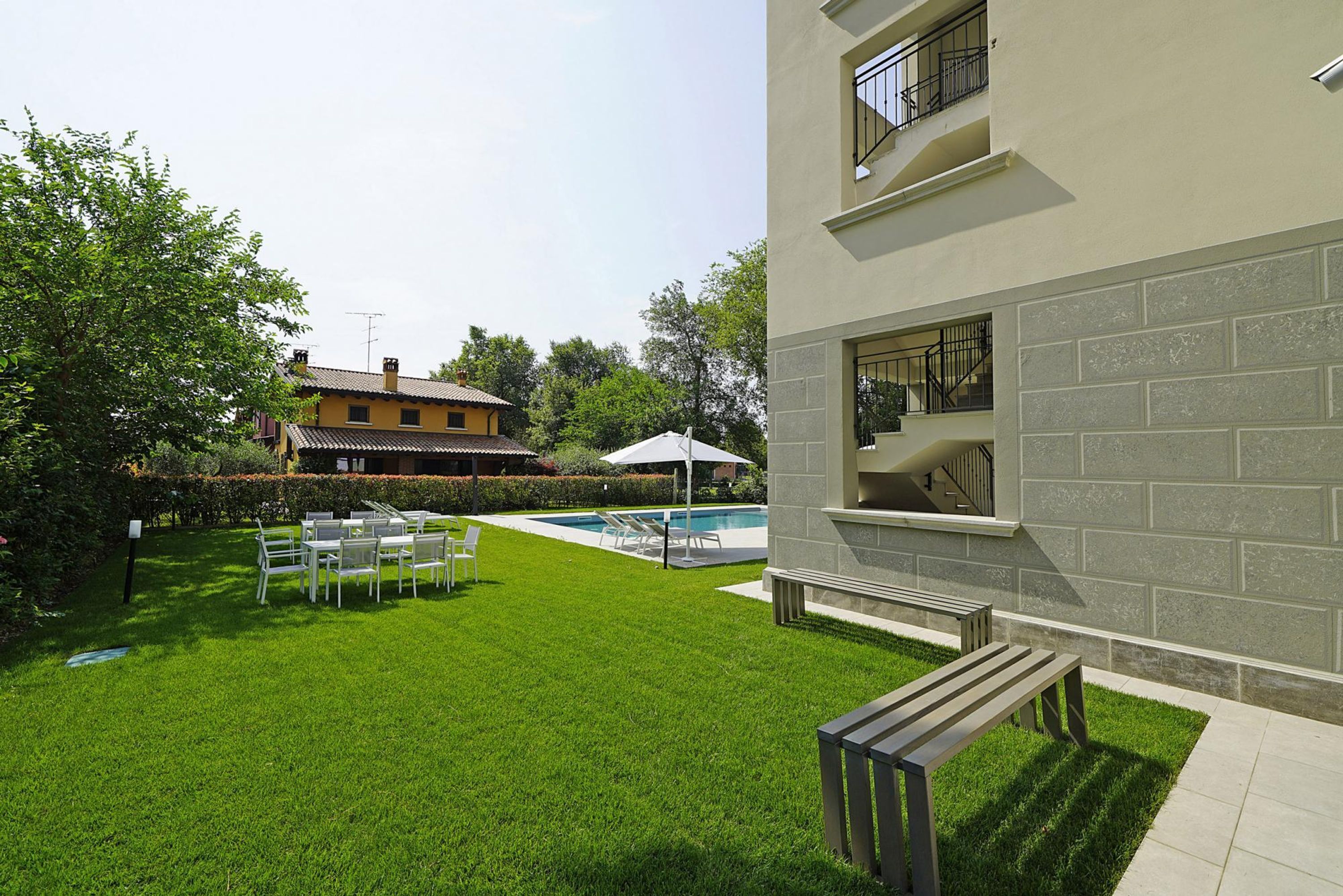 A well-maintained backyard with a swimming pool, a patio with chairs and a table, and a stone wall.