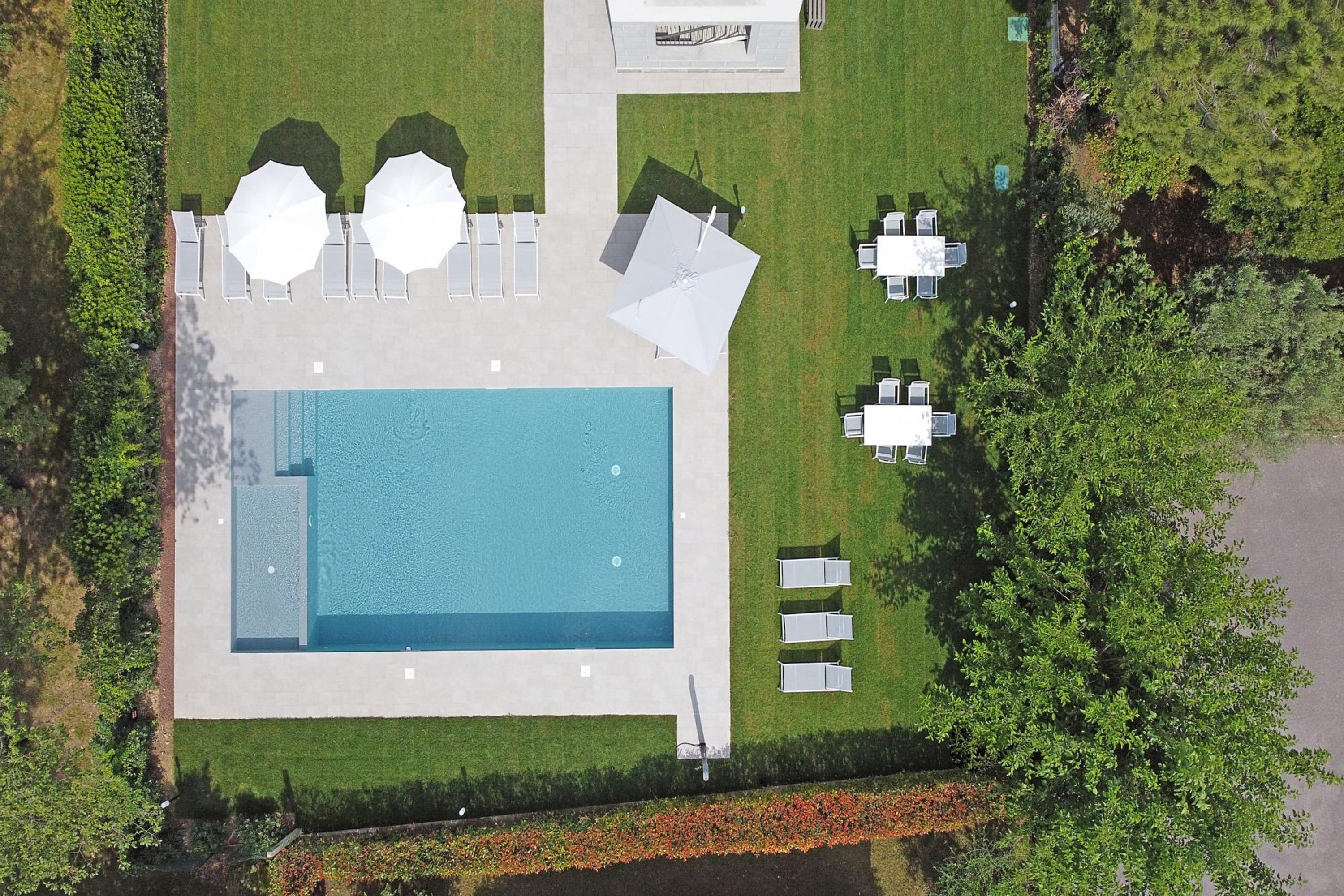 Luftaufnahme eines Poolbereichs mit Liegestühlen und Sonnenschirmen.