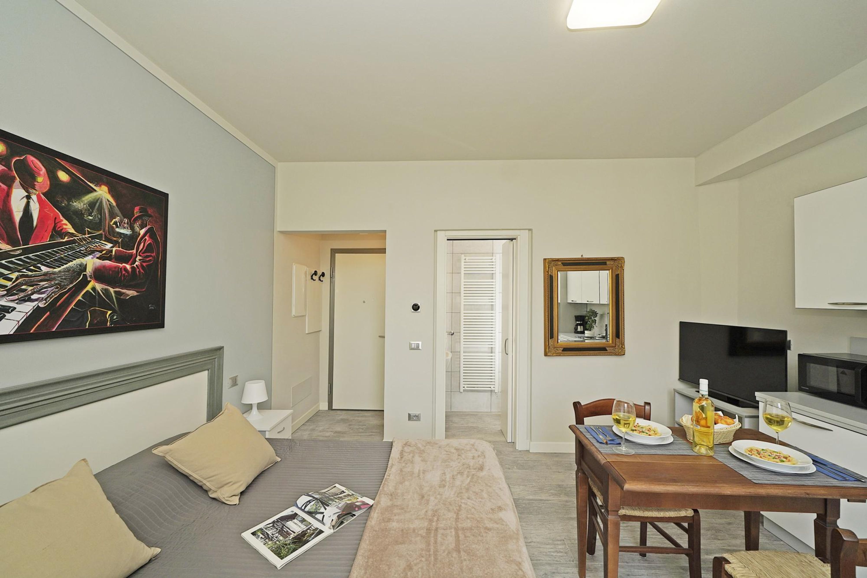 A hotel room with a bed, a dining table with chairs, a television, and a painting on the wall.