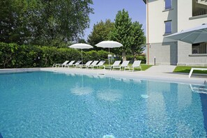 A clear swimming pool with lounge chairs and umbrellas, surrounded by greenery and a building. - Villa Caterina 8 - LOC (Desenzano del Garda)