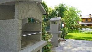 Une structure en pierre comprenant un banc et une petite tour, le tout entouré d’une pelouse bien entretenue et d’une zone pavée.