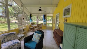 Eine überdachte Veranda mit Korbmöbeln, einem Deckenventilator und Blick ins Freie.
