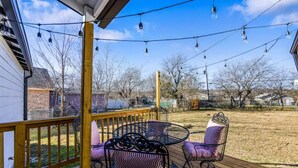 Une terrasse en bois avec une table et des chaises en métal, entourée d’une balustrade en bois.