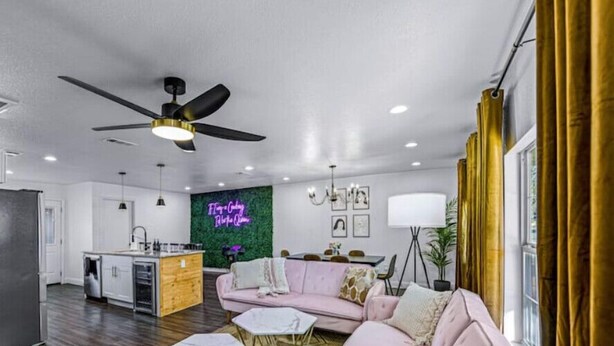 Un salon moderne avec un canapé rose, un ventilateur de plafond et un néon mural.