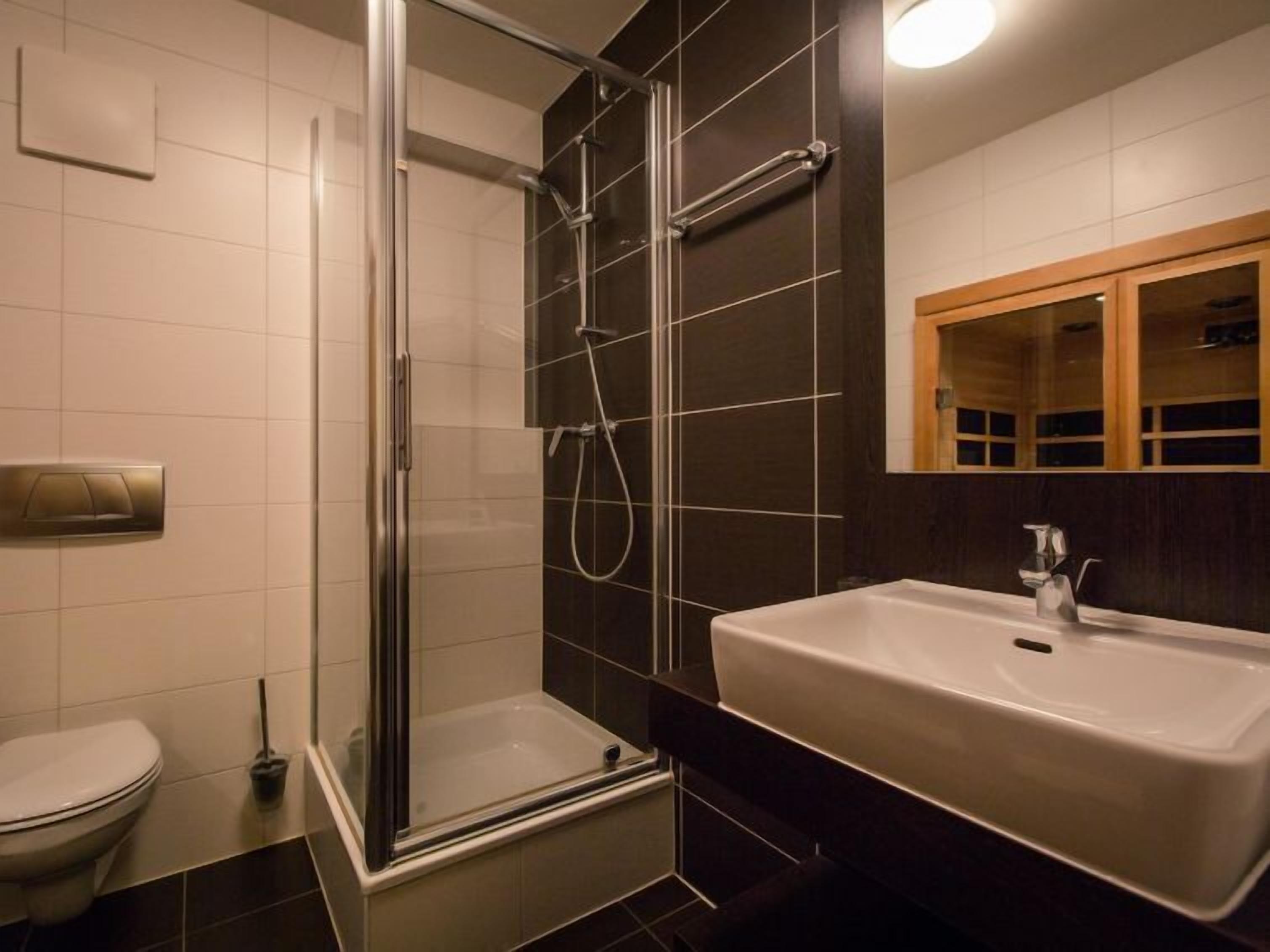 Ein modernes Badezimmer mit einer ein Glasfachwerk umschlossenen Dusche, einem weißen Waschbecken und einem Spiegel mit Holzrahmen.