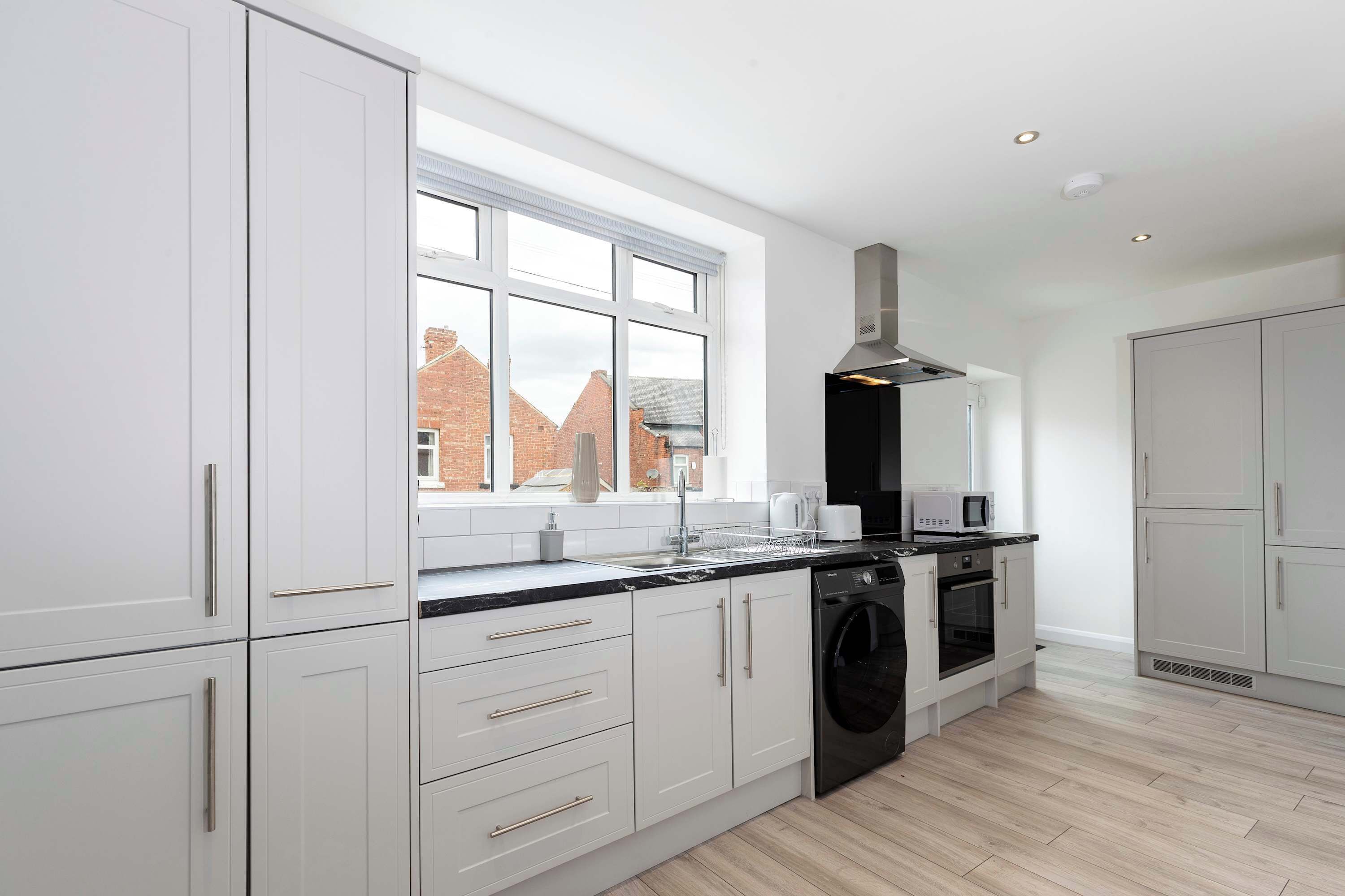 A modern kitchen with white cabinetry, a built-in oven, and a window overlooking a brick building.