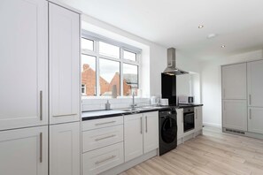A modern kitchen with white cabinetry, a built-in oven, and a window overlooking a brick building.
