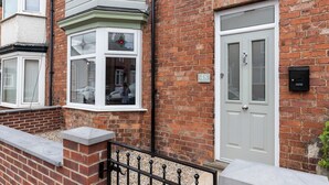 A residential building with a brick facade, a white door, and a bay window with a stained glass design. - Stylish 3 Bed House With TVs in Each Bedroom (Darlington)