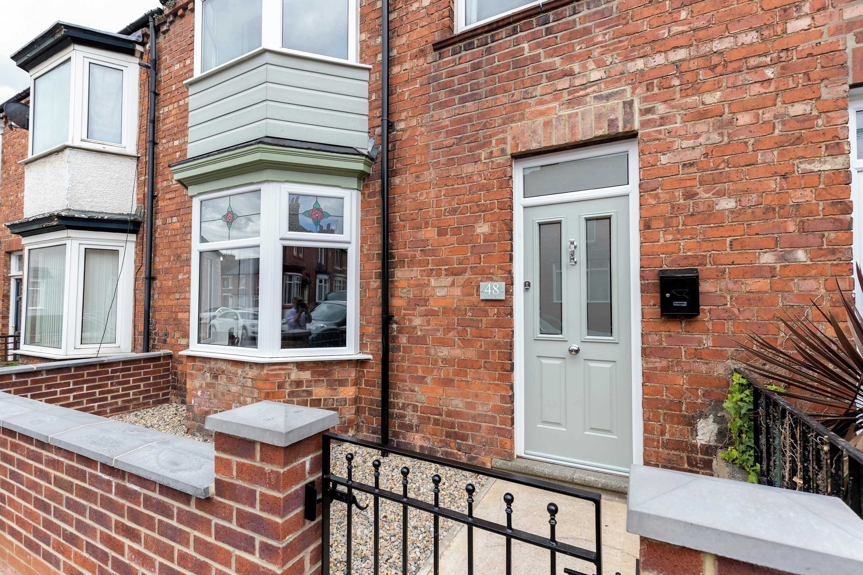 A residential building with a brick facade, a white door, and a bay window with a flower design.