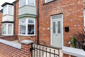 A residential building with a brick facade, a white door, and a bay window with a flower design.