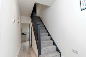 A staircase with carpeted steps and a black handrail leading to an upper floor. - Stylish 3 Bed House With TVs in Each Bedroom (Darlington)