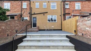 A residential building with a brick facade, a front door, and a small outdoor seating area with a table and chairs.