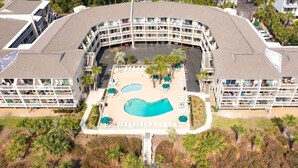 A hotel with a central swimming pool, multiple balconies, and a parking area.