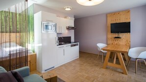 Eine moderne Küche mit weißen Schränken, einer Mikrowelle und einem Spülbecken. Ein Holztisch mit zwei Stühlen und einem an der Wand montierten Fernseher sind ebenfalls vorhanden.