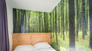 Ein Schlafzimmer mit großem Wandgemälde von einem Wald, einem Holzkopfteil und weißer Bettwäsche.