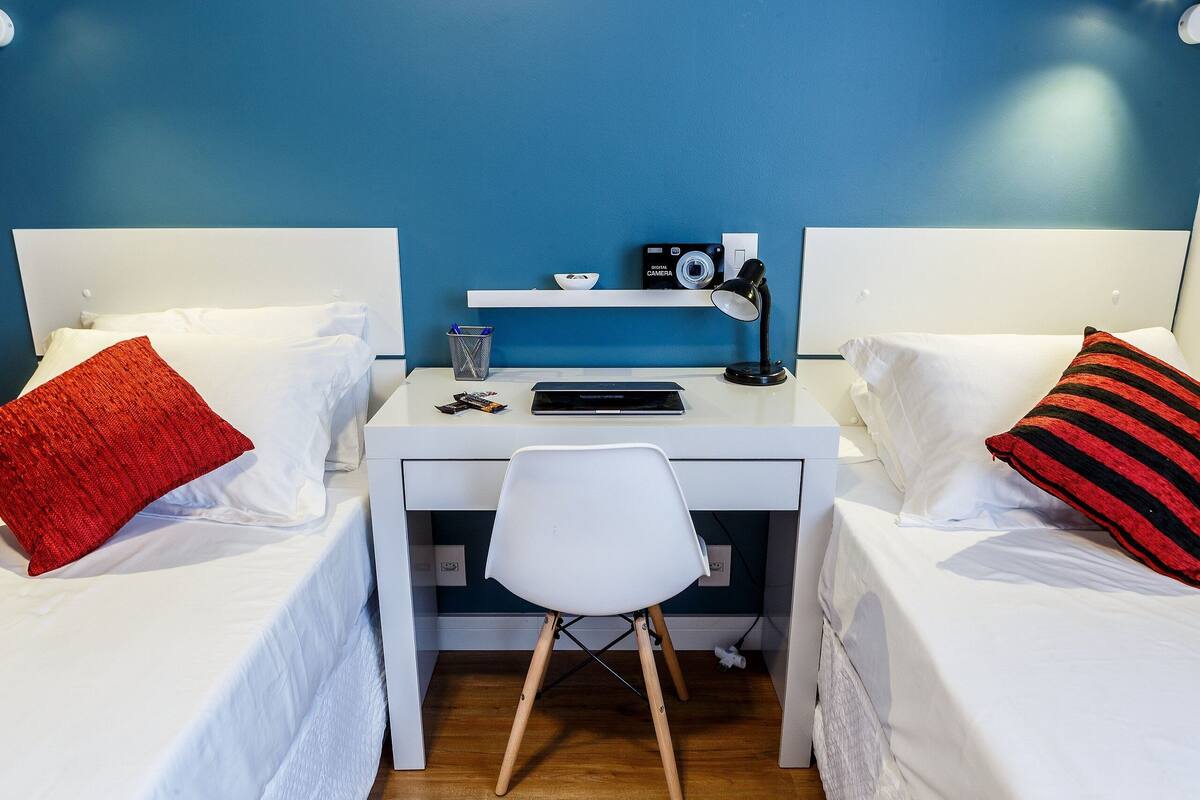 A twin room with a desk, two beds, a chair, a camera, and a lamp.