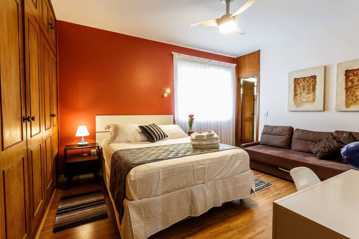 A hotel room with a bed, a nightstand, a desk, a sofa, and a ceiling fan.