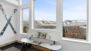 Ein Zimmer mit einer Sitzbank, einem Skiständer und Blick auf Berge sowie Gebäude durch große Fenster.