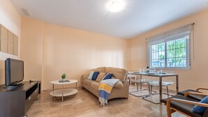 Un salon moderne comprenant un canapé, un téléviseur, une table à manger avec des chaises et une fenêtre donnant sur un paysage arboré.