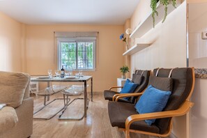 Uma sala de estar moderna com área de jantar, com um sofá, cadeiras, uma mesa posta com copos e uma janela com vista para o verde.