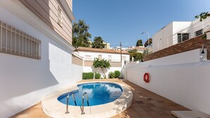 Une piscine dotée d’une plage carrelée, entourée de murs blancs et d’un mur de briques d’un côté.