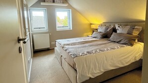 A bedroom with a sloped ceiling, a bed with multiple pillows, two windows, and a radiator. - Schöne Ferienwohnung für Geschäftsleute und Paare (Osnabrück)