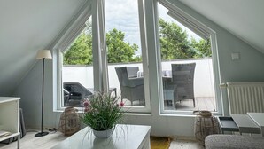 A room with a sloped ceiling, large windows, wicker furniture, and a white table. - Schöne Ferienwohnung für Geschäftsleute und Paare (Osnabrück)