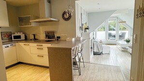 A modern kitchen with a central island, wooden flooring, and a view into a dining area with natural light. - Schöne Ferienwohnung für Geschäftsleute und Paare (Osnabrück)
