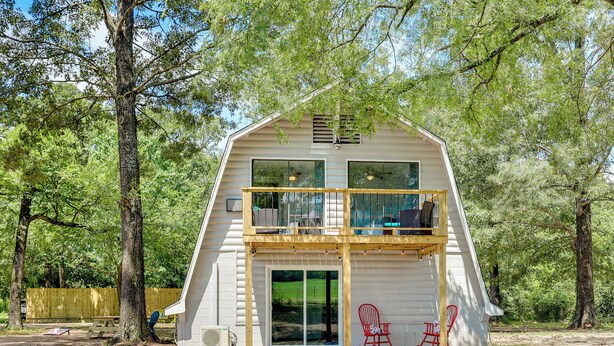 A two-story cabin with a balcony, large windows, and a sliding glass door. - Family-Friendly Broken Bow Home w/ Grill! (Broken Bow)