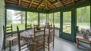 A covered porch with a wooden table and chairs, large windows, and a view of the outdoors. - Beach & Kayaks: Waterfront Cabin on Lake Pleasant! (Speculator)