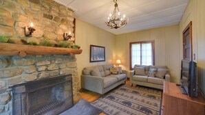 A cozy living room with a stone fireplace, two sofas, a television, and a chandelier. - Beach & Kayaks: Waterfront Cabin on Lake Pleasant! (Speculator)