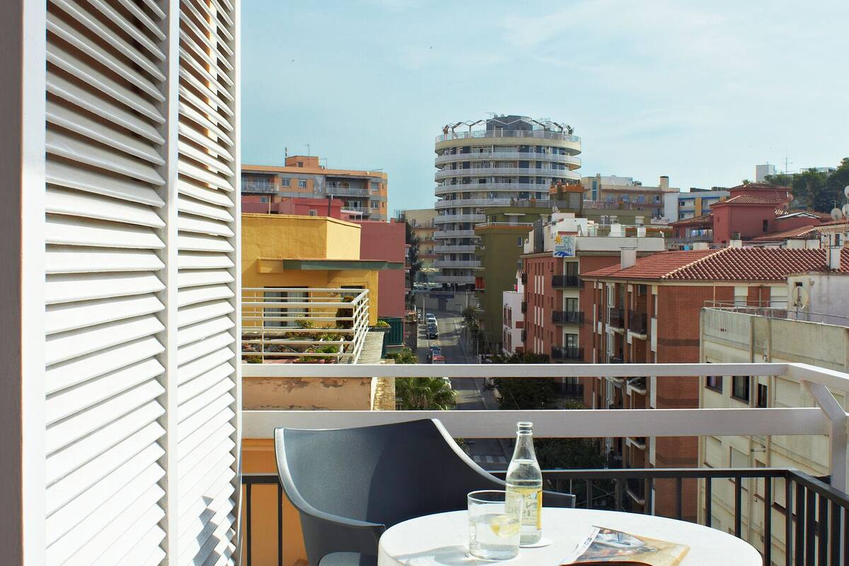 En balkon med et rundt bord og to stole, udsigt over et bybillede med forskellige bygninger.