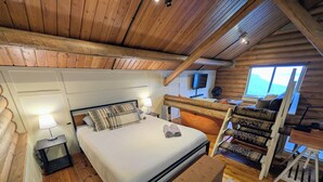 A wooden cabin bedroom with a bed, bedside lamp, and a view of the outdoors. - Classic log cabin with stunning views! (Irwin)