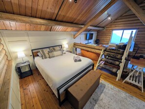 A wooden cabin bedroom with a bed, bedside lamp, and a view of the outdoors. - Classic log cabin with stunning views! (Irwin)