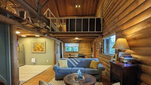 A cozy log cabin interior with a living room featuring a blue sofa, a coffee table, and a dining area with a table and chairs. - Classic log cabin with stunning views! (Irwin)