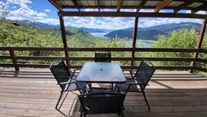 A wooden deck with a table and chairs overlooking a mountainous landscape and a lake. - Classic log cabin with stunning views! (Irwin)