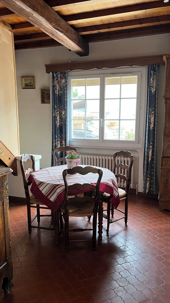 A dining area with a table set for four, wooden chairs, a floral vase, and a window with curtains.