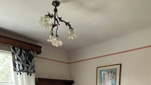 Ein Zimmer mit zwei Betten, einem Heizkörper, einem Fenster mit Vorhängen, einem Gemälde an der Wand und einer Chandelieber.