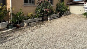 Ein Haus mit einem Schotterweg, einer Garage und einem Garten mit verschiedenen Pflanzen und Blumen.