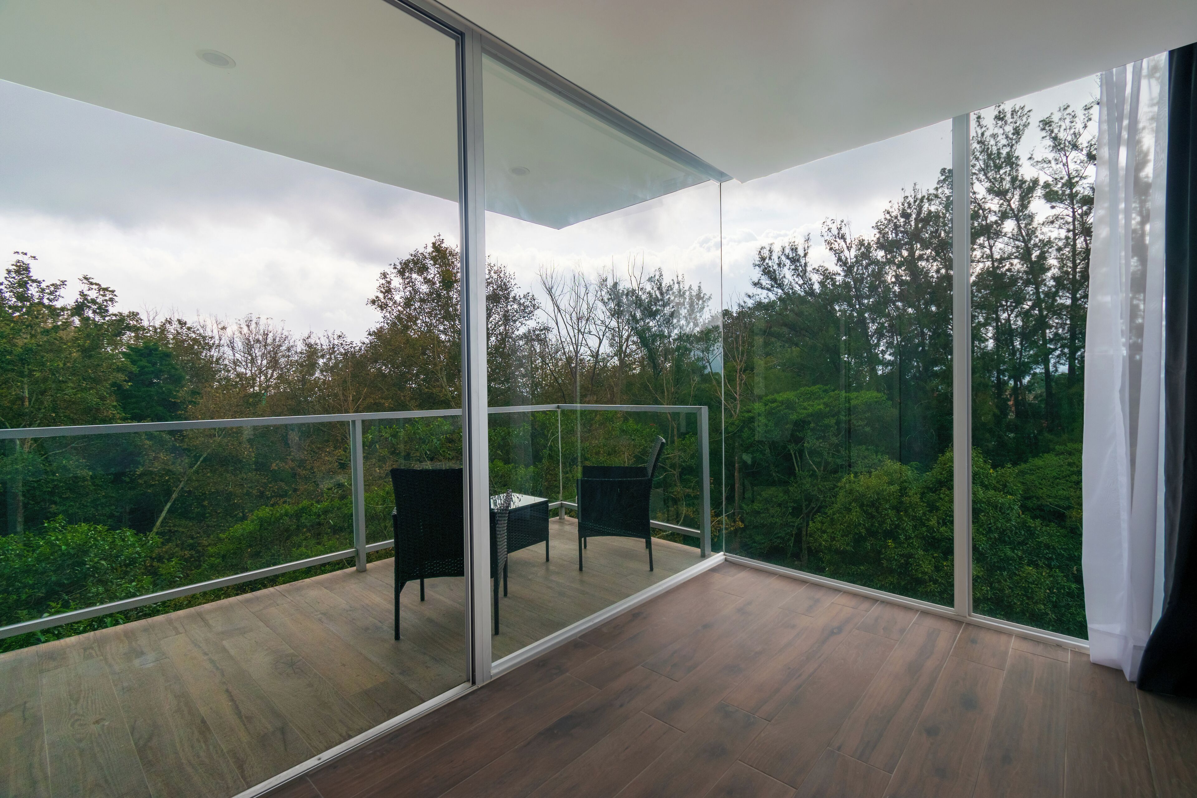 A modern balcony with a glass railing, a wooden floor, and two chairs.