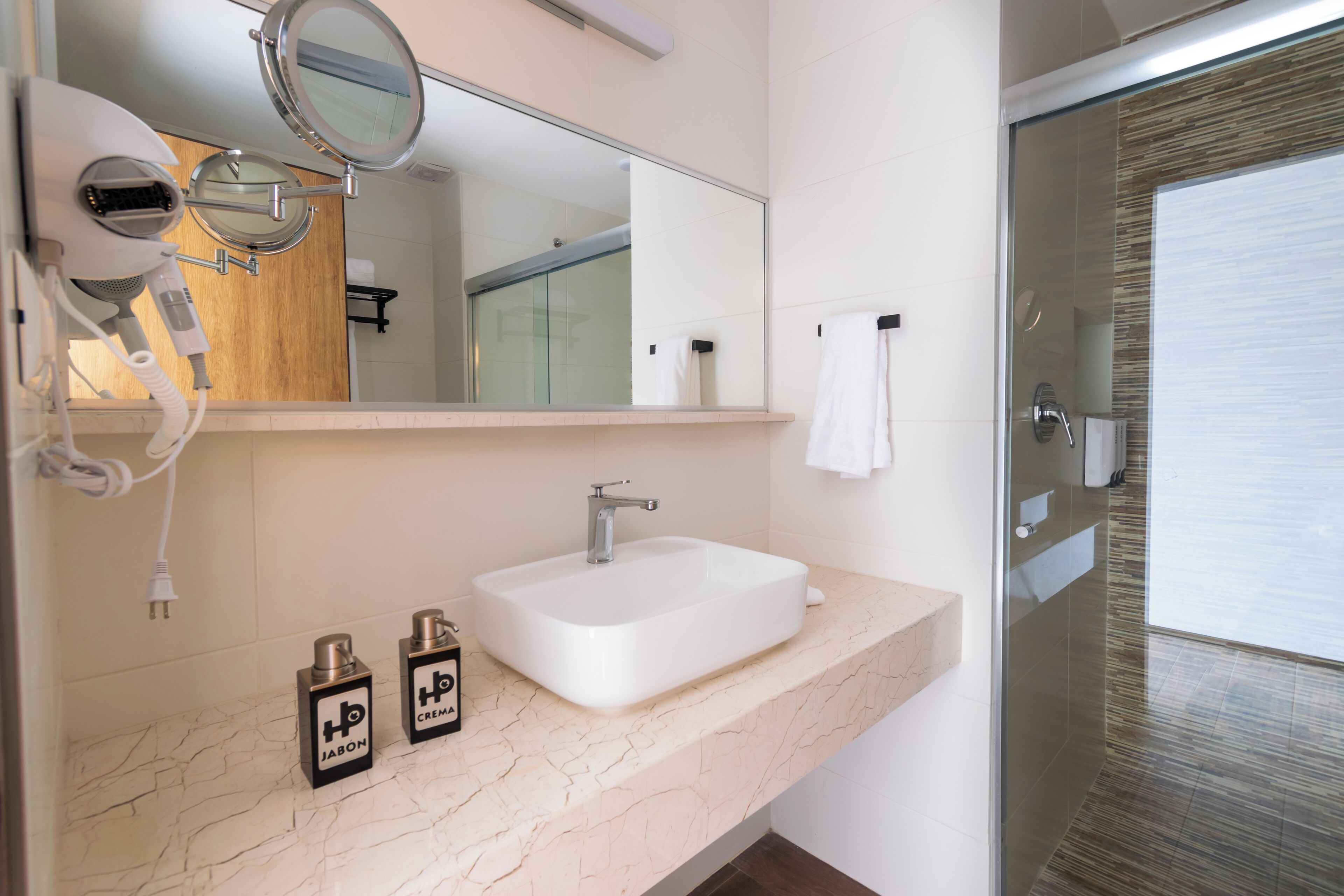 A bathroom with a white sink, a mirror, a hairdryer, and two bottles of hair product.