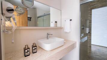 A bathroom with a white sink, a mirror, a hairdryer, and two bottles of hair product.