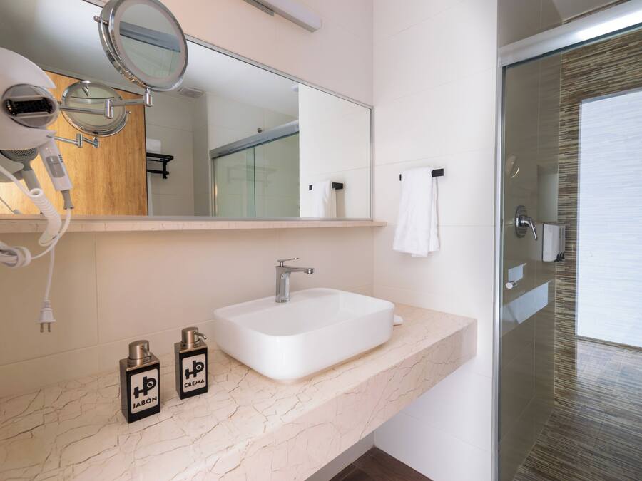 A bathroom with a white sink, a mirror, a hairdryer, and two bottles of hair product.