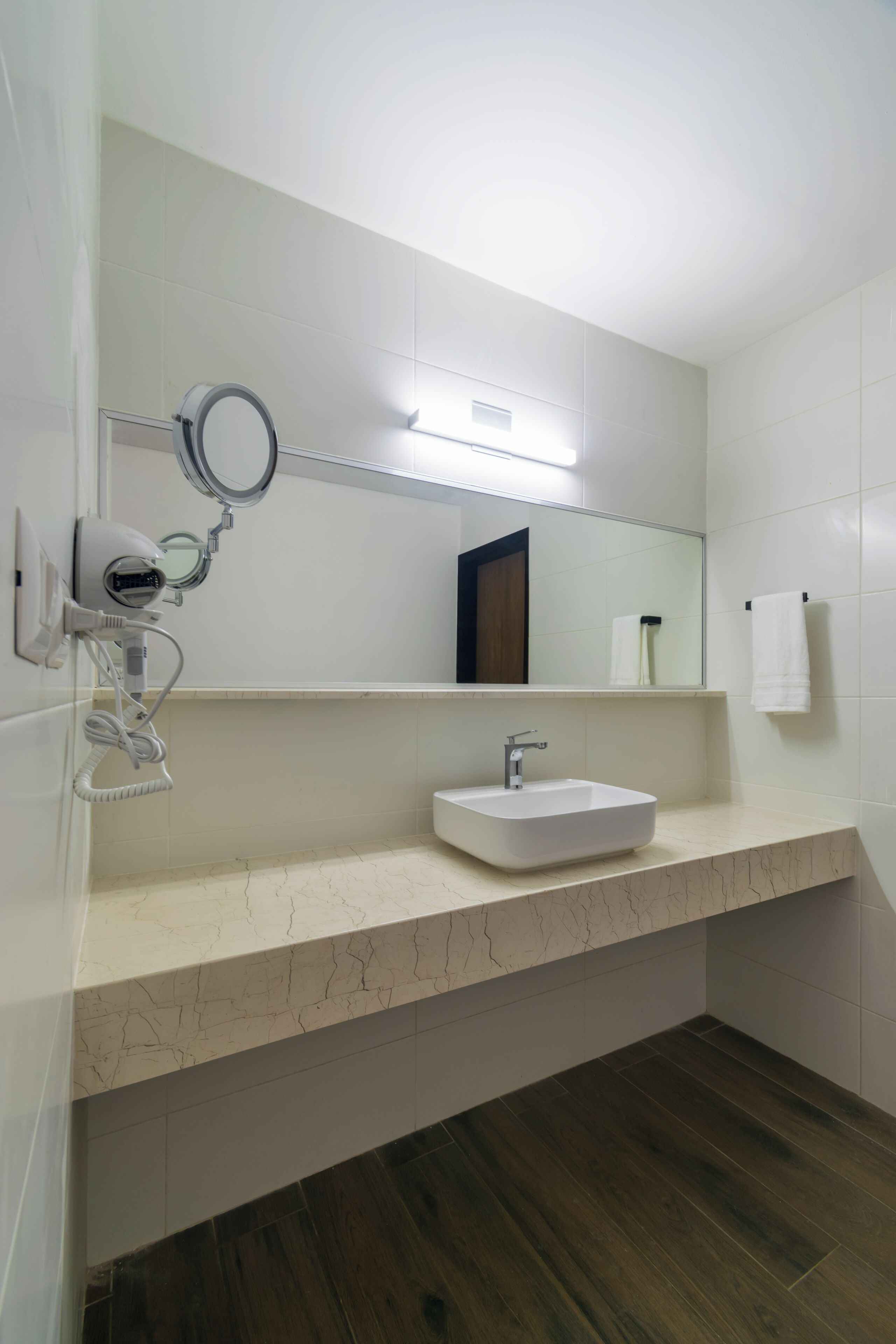 Un baño con lavamanos blanco, un espejo y un secador de pelo montado en la pared.